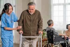 Older adults and staff walk through a bright assisted living hallway with handrails, clear paths, and emergency signage.